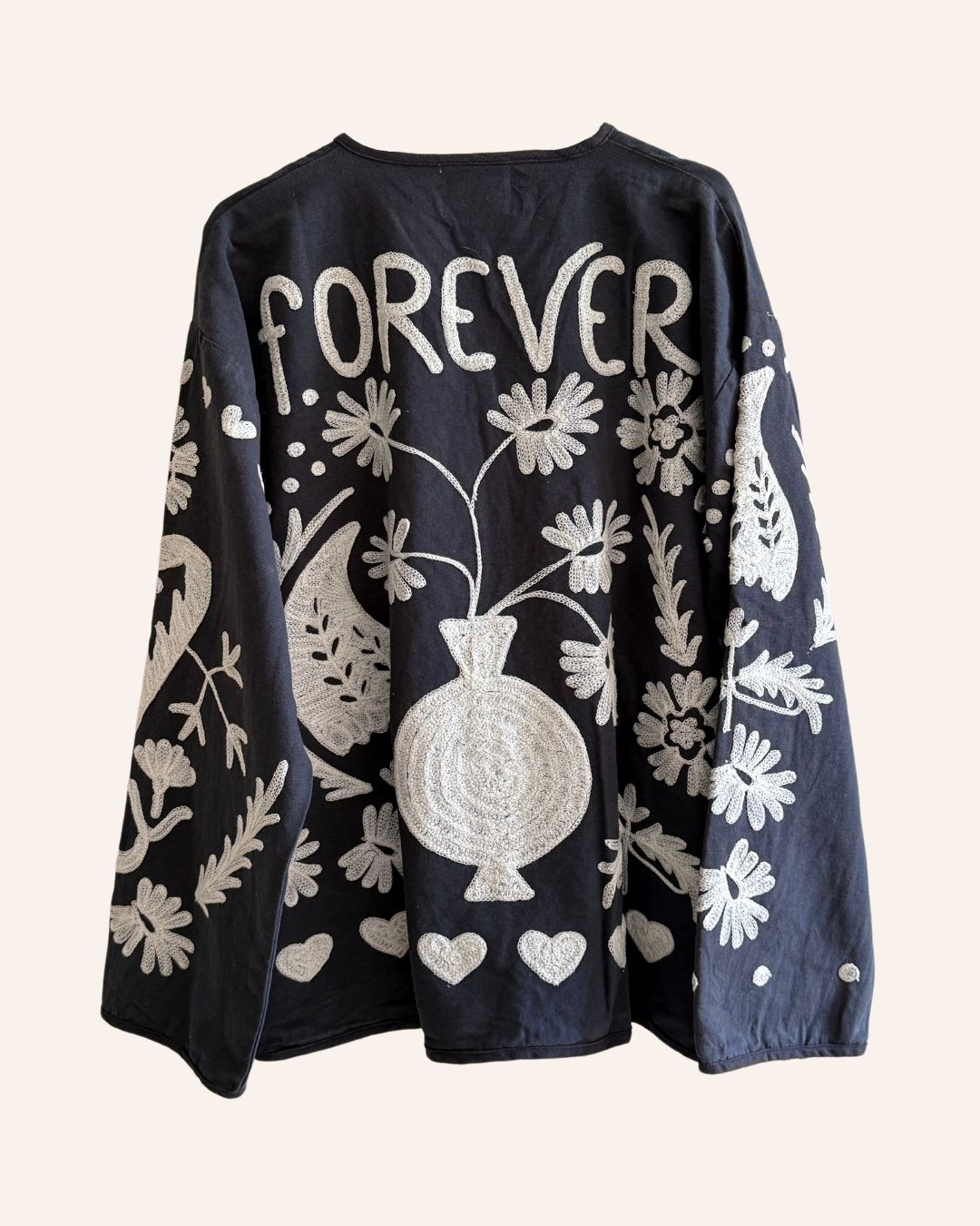 Back of black embroidered jacket with ivory floral and heart motifs and “FOREVER” text