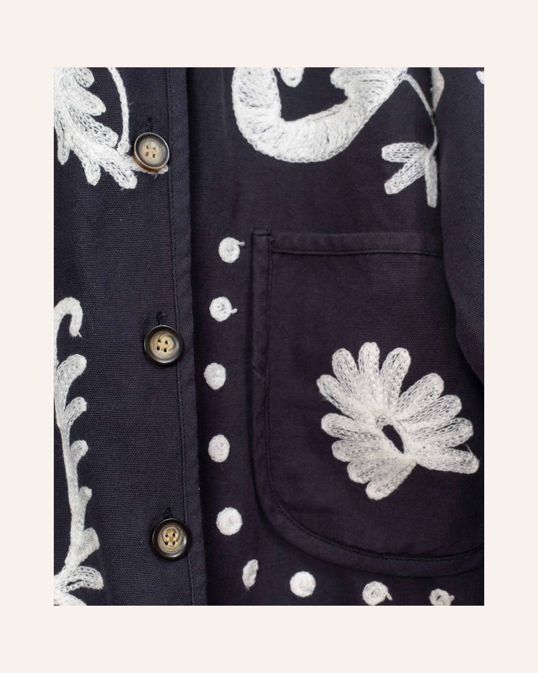 Hand-embroidered navy cotton jacket featuring intricate white floral and heart motifs with playful, folk-inspired details.