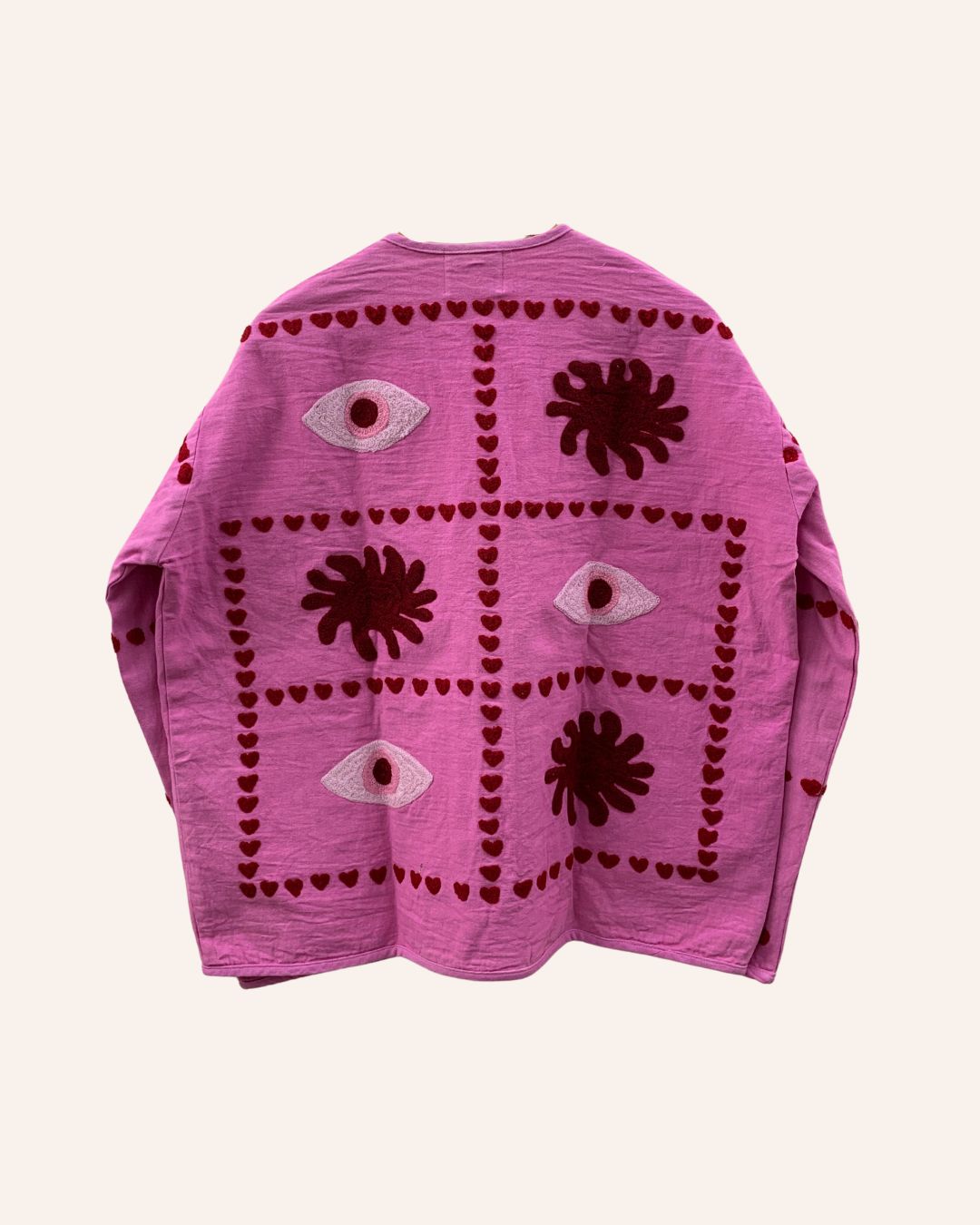 Back view of a pink embroidered jacket featuring bold eye and sunburst patterns framed with red heart details.