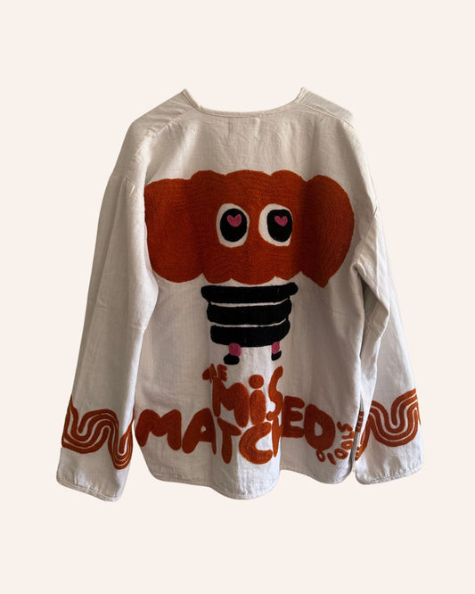 Back view of a white cotton jacket featuring a large fuzzy orange elephant with heart-shaped eyes and bold “The Mismatched Studio” embroidery.