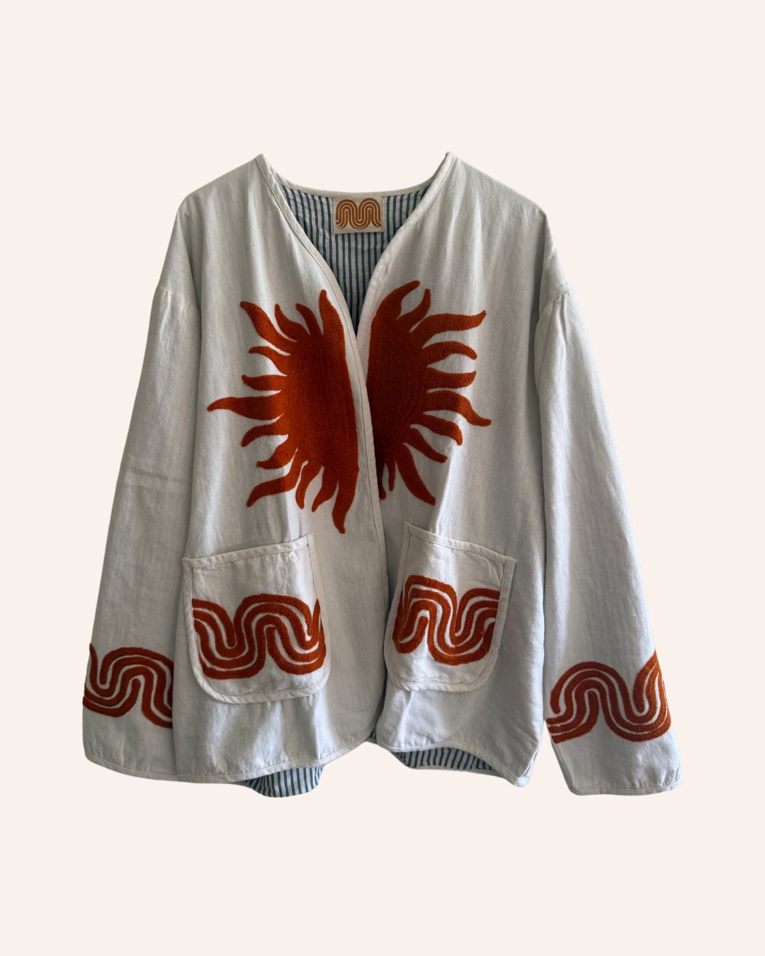 Front view of a white cotton jacket with an embroidered orange sunburst design and wavy rust trims on the pockets and sleeves.