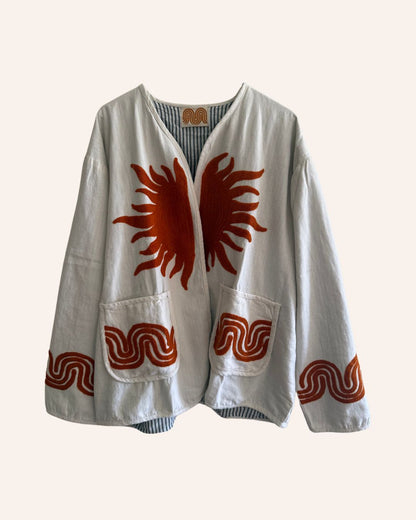 Front view of a white cotton jacket with an embroidered orange sunburst design and wavy rust trims on the pockets and sleeves.