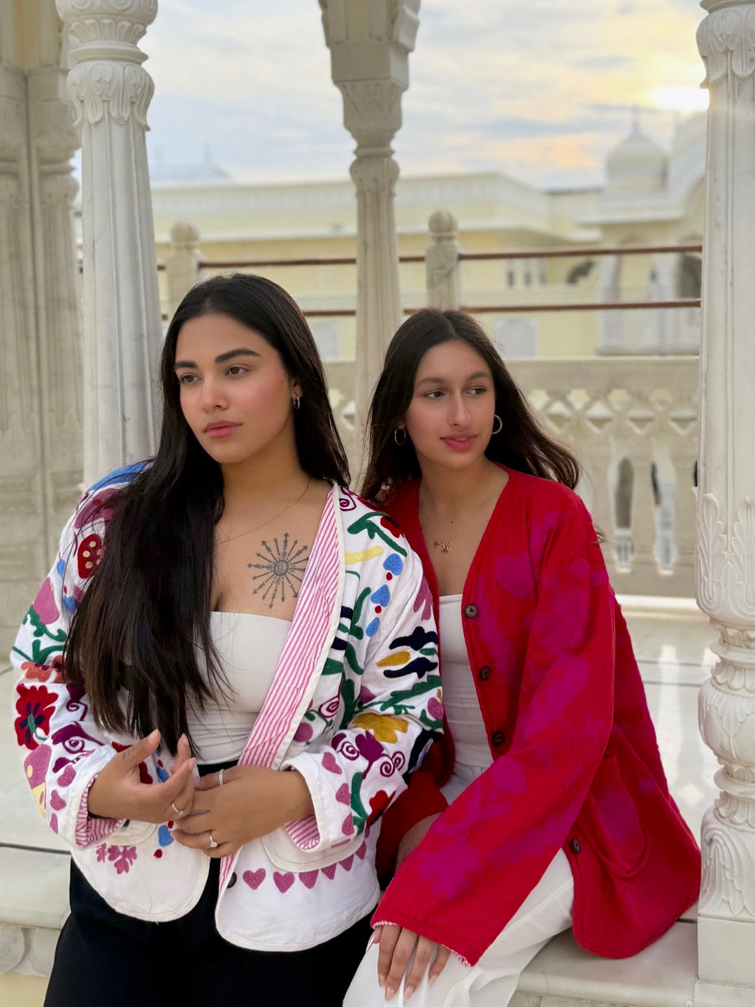 Two women sitting with cool jackets on  with architectural columns and a scenic background.