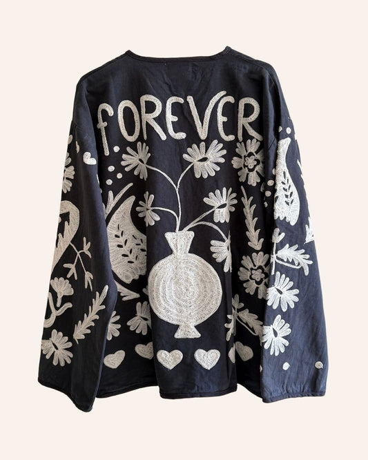 Back of black embroidered jacket with ivory floral and heart motifs and “FOREVER” text