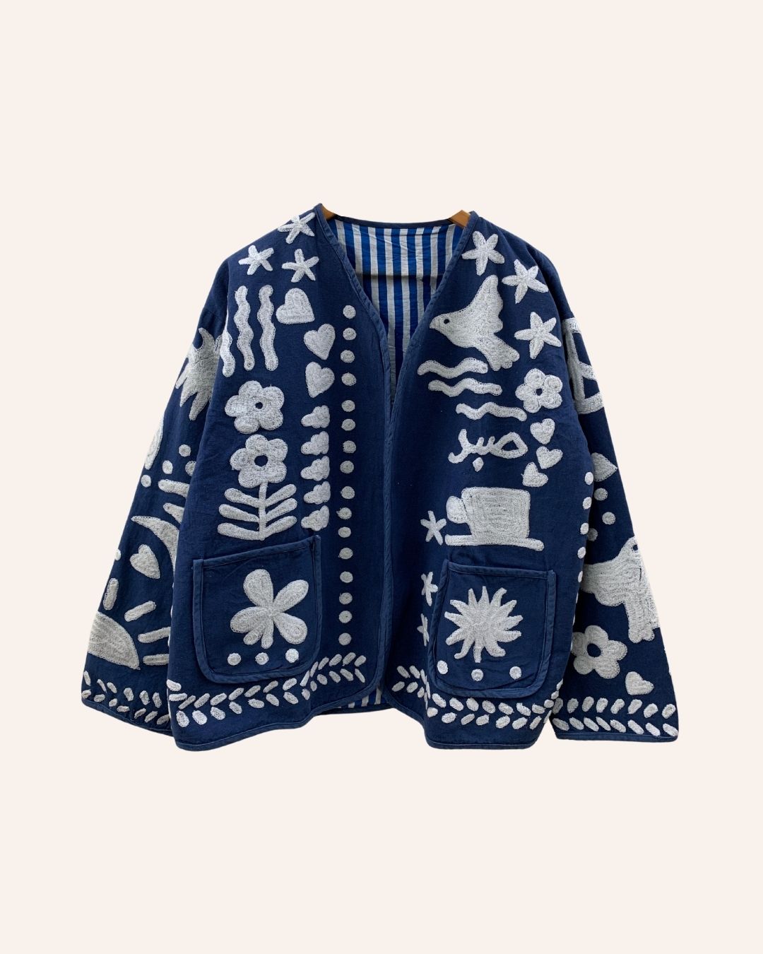 Front view of navy blue embroidered jacket with floral, bird, and Arabic motifs in white thread, featuring patch pockets and open front design.