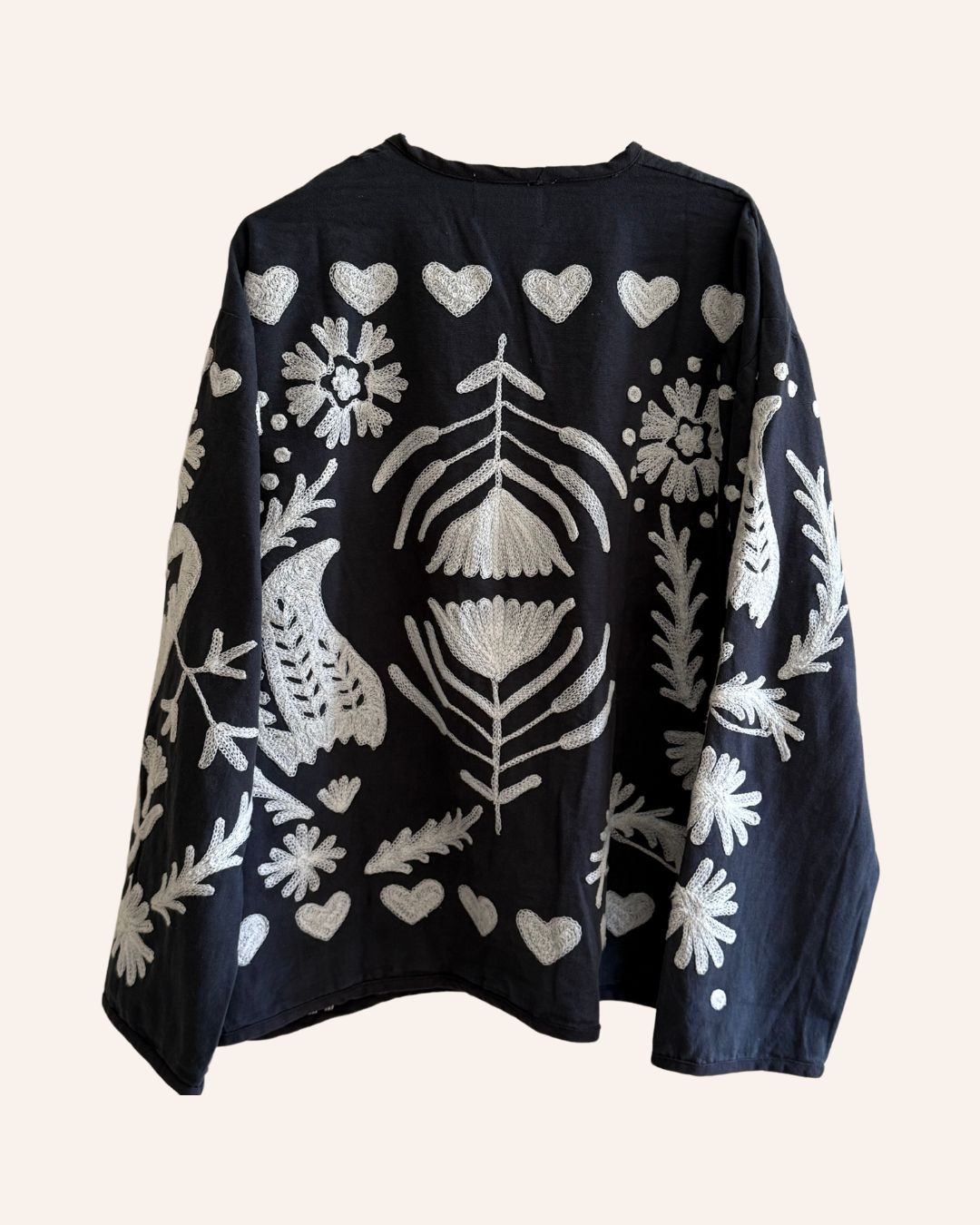 Back of black jacket with intricate ivory embroidery featuring bold central floral motif and heart border