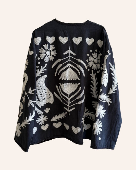 Back of black jacket with intricate ivory embroidery featuring bold central floral motif and heart border