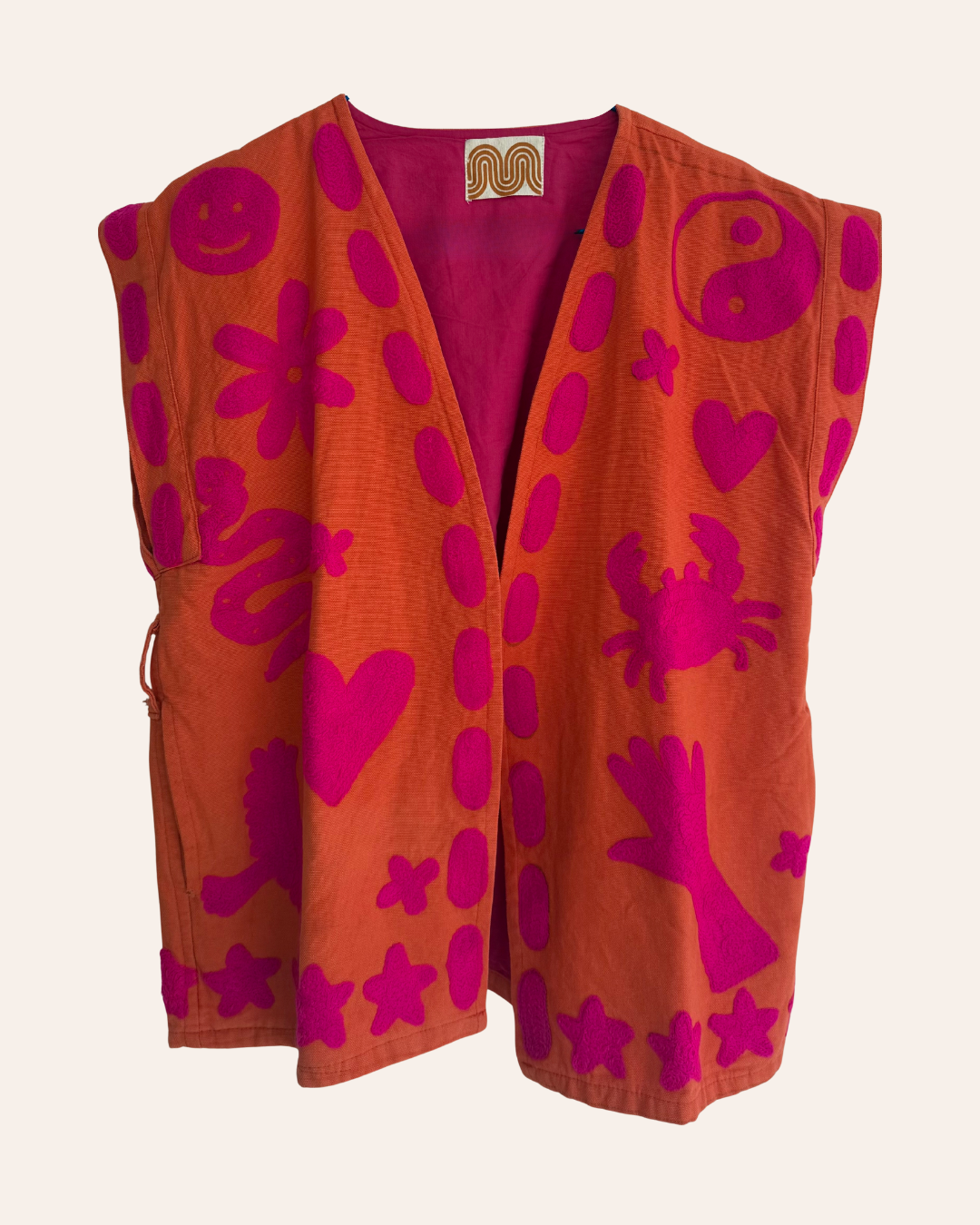 Hand-embroidered orange summer vest with pink playful symbols including crab, heart, flower, and yin-yang.