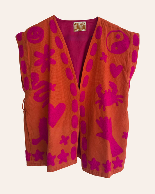 Hand-embroidered orange summer vest with pink playful symbols including crab, heart, flower, and yin-yang.