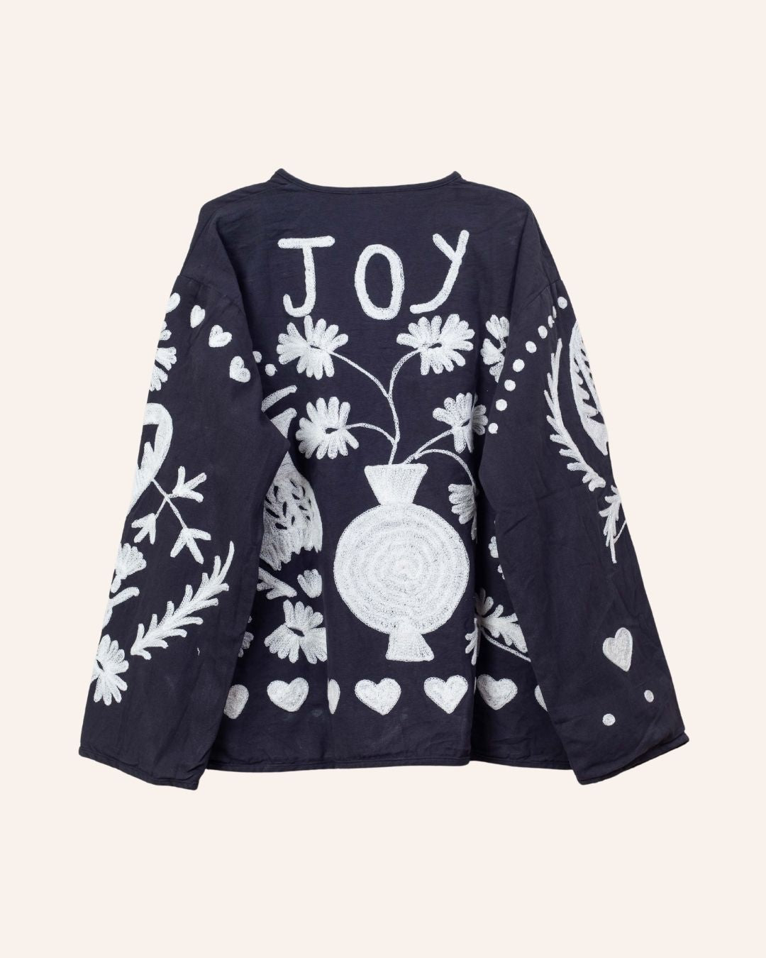 Hand-embroidered navy cotton jacket with white hearts, florals, and JOY motif on the back, inspired by playful folk-art storytelling.