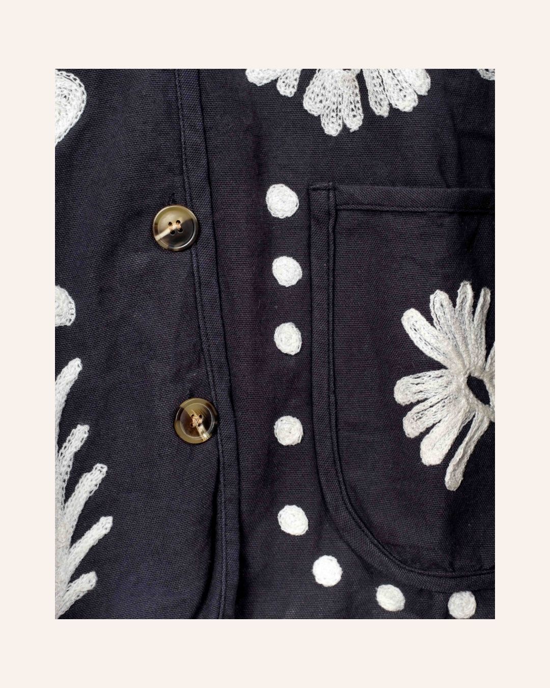 Hand-embroidered navy cotton jacket with white hearts, florals, and JOY motif on the back, inspired by playful folk-art storytelling.