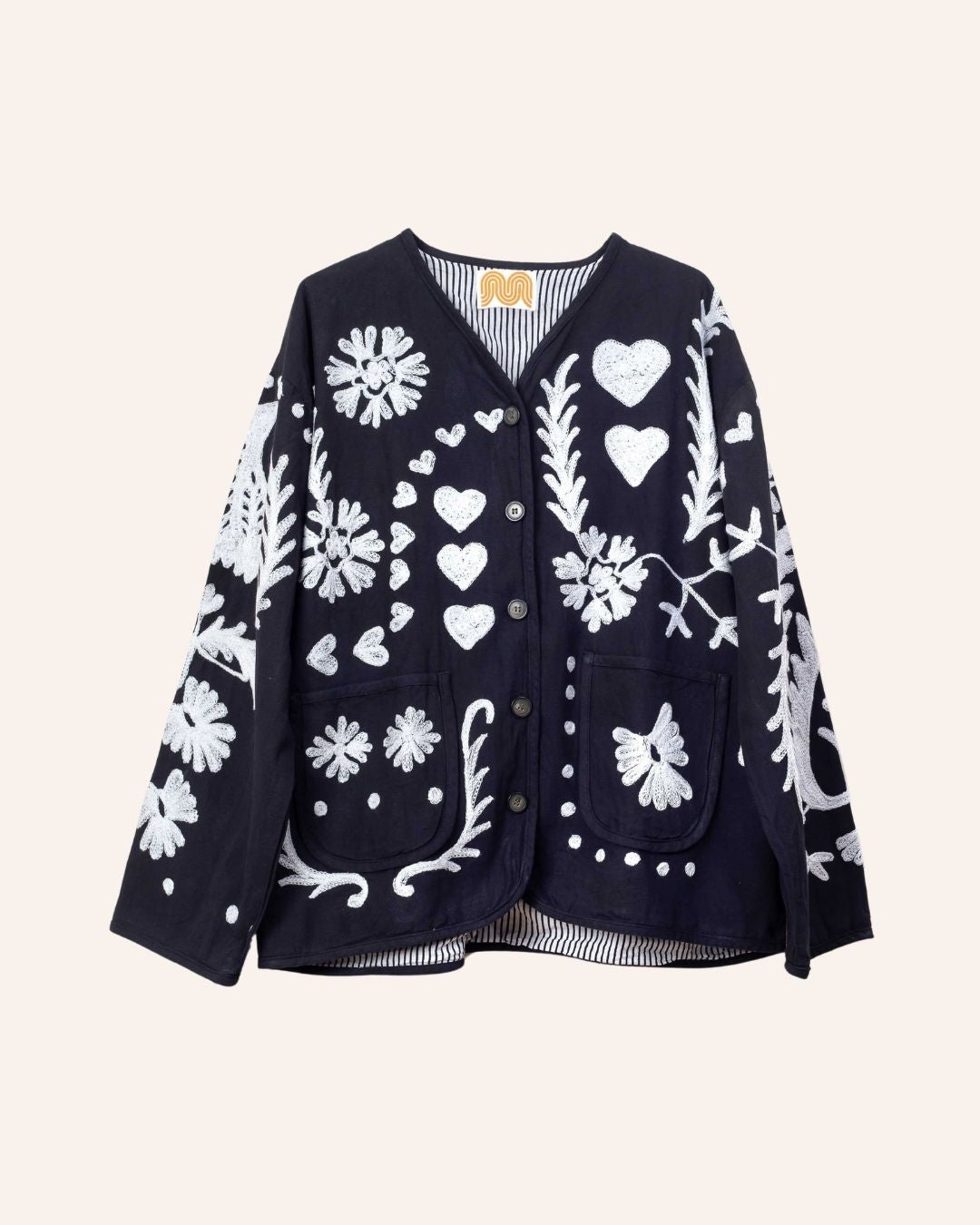 Hand-embroidered navy cotton jacket with white hearts, florals, and JOY motif on the back, inspired by playful folk-art storytelling.