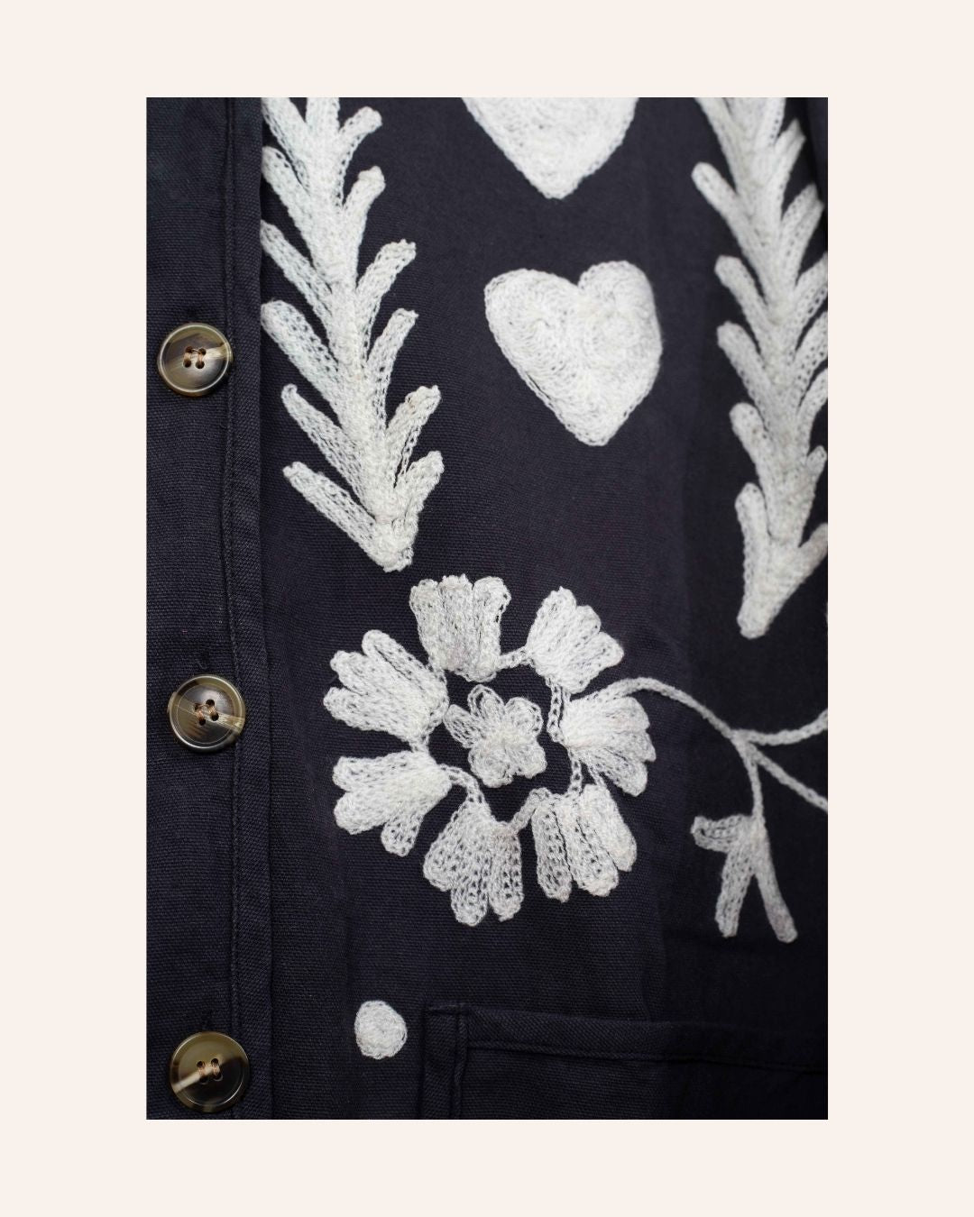 Hand-embroidered navy cotton jacket with white hearts, florals, and JOY motif on the back, inspired by playful folk-art storytelling.