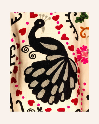 Cream cotton jacket hand-embroidered with black peacock, pink florals, red hearts, and swirling folk-style vines.
