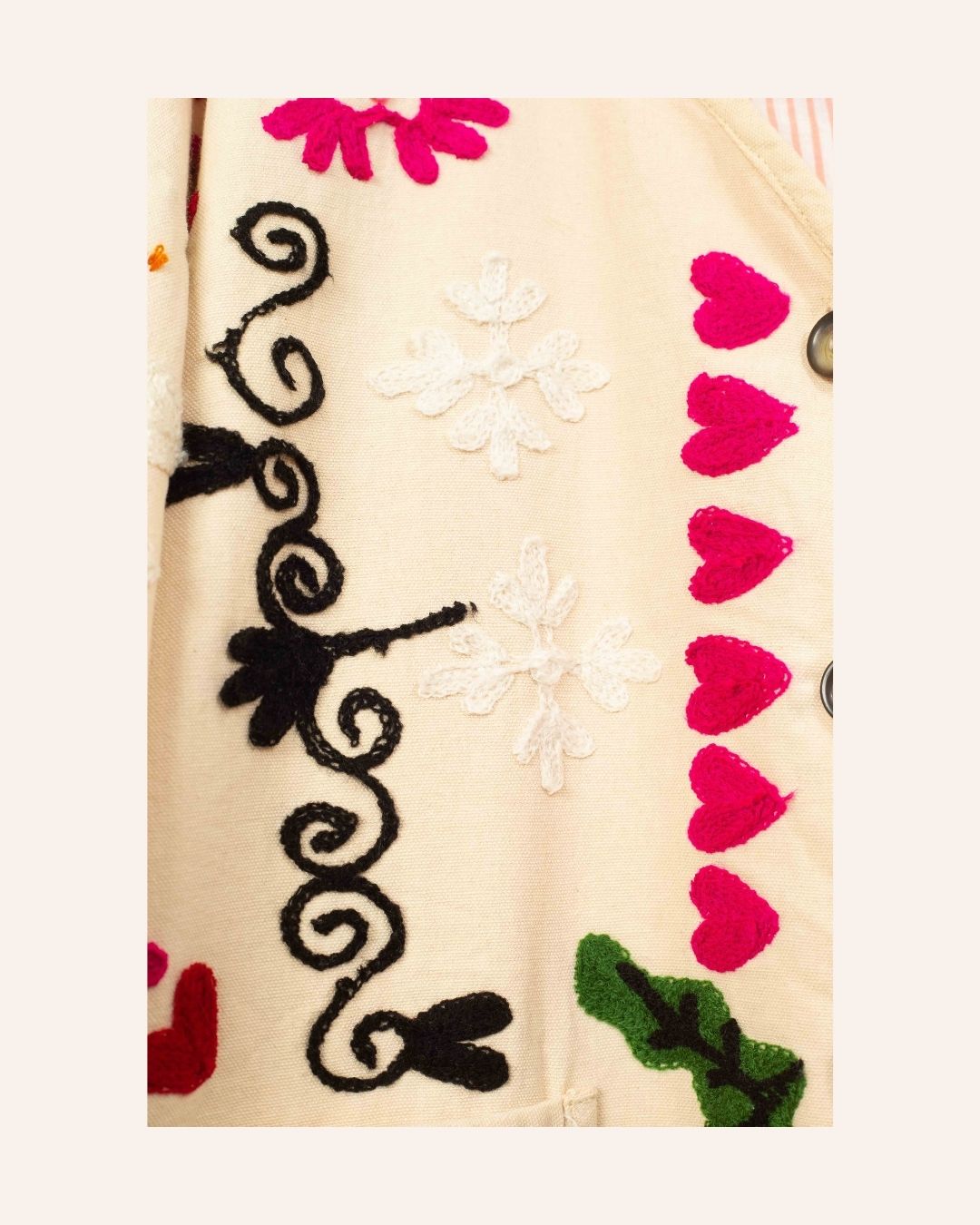 Cream cotton jacket hand-embroidered with black peacock, pink florals, red hearts, and swirling folk-style vines